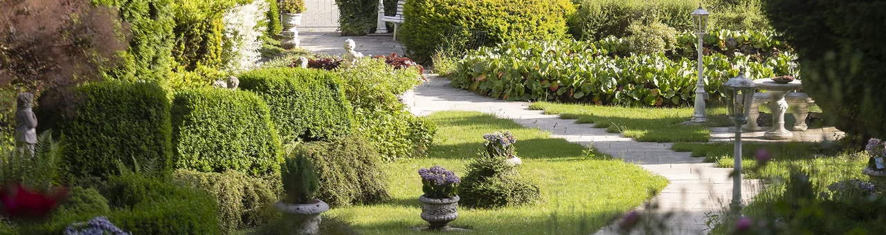 Gepflegte Gartenanlage im SchlossFUN (Schlössle Seeburg) mit geschwungenen Wegen, kunstvoll geschnittenen Hecken, Zierpflanzen und historischen Gartenfiguren.