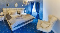 Elegantes Doppelzimmer in Blau mit edlem Kronleuchter, gepolstertem Bett und stilvollen Vorhängen.