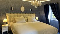Schlafzimmer der Suite Nachtigall mit großem Bett, blauer Wandverkleidung und goldenen Spiegeln