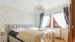 Helles Doppelzimmer mit großem Bett, elegantem Kronleuchter, feiner Tapete und lichtdurchfluteten Fenstern mit Vorhänge