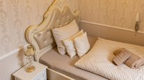 Elegantes Einzelzimmer mit gepolstertem, verziertem Kopfteil, heller Bettwäsche und klassischer Tapete in warmen Beigetönen.