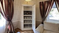 Wohnzimmer der Suite Nachtigall im Schloss Seeburg mit stilvollem Weinschrank, Gläsern und edlen Vorhängen.