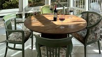 Heller Wintergarten der Suite Nachtigall im Schlössle Seeburg mit rundem Holztisch, grünen Stühlen und Zugang zur Terrasse.