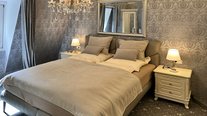 Doppelbett im zweiten Schlafzimmer der Suite Nachtigall mit grauer Tapete und Nachttischen