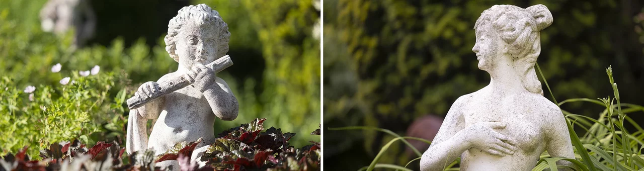Historische Gartenfiguren im Park des SchlossFUN (Schlössle Seeburg): links eine Puttenfigur mit Flöte, rechts eine klassische Frauenstatue zwischen Blumen und Grünpflanzen.